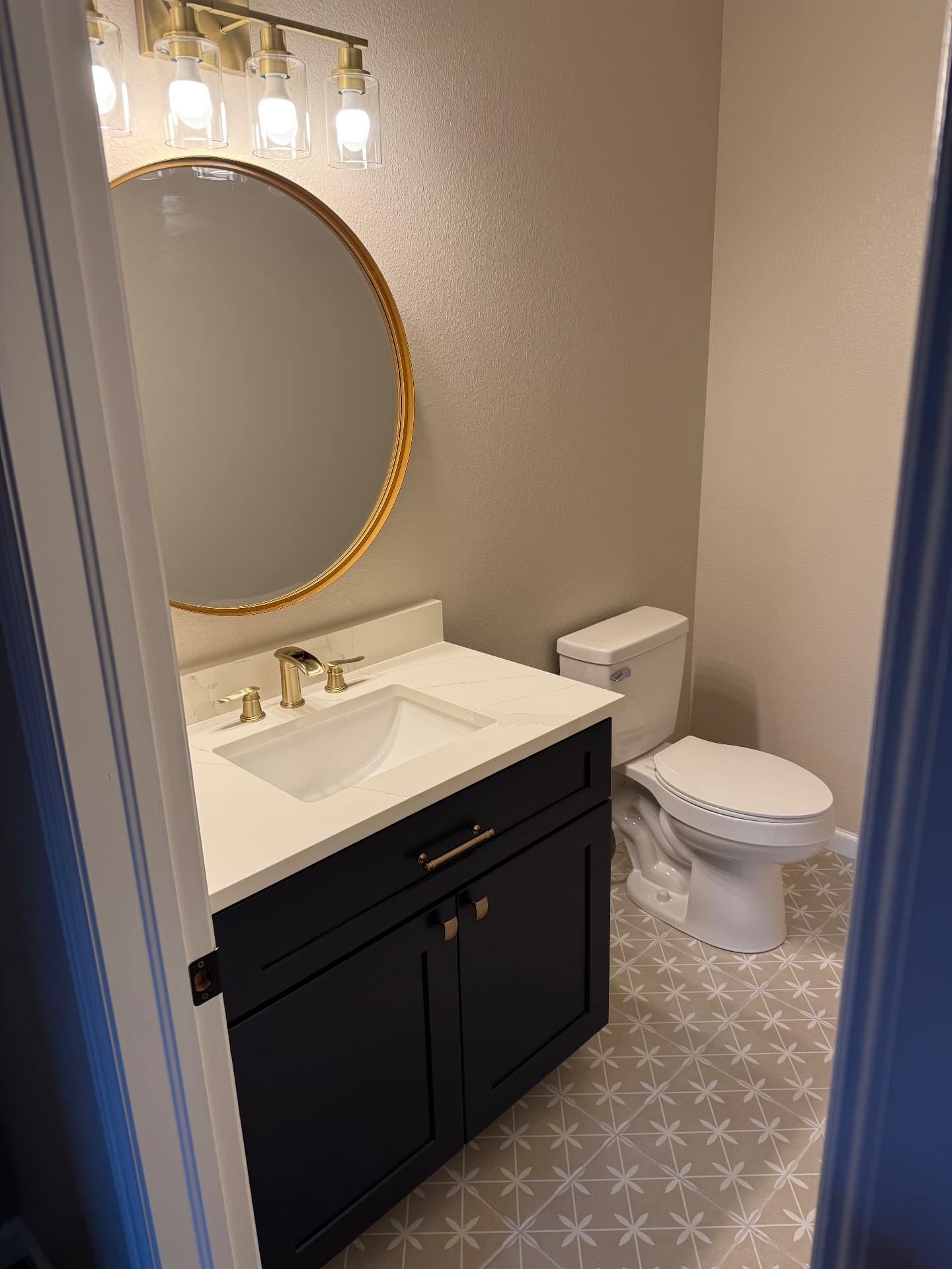 Renovated powder room with navy vanity, round brass mirror, and patterned floor tile