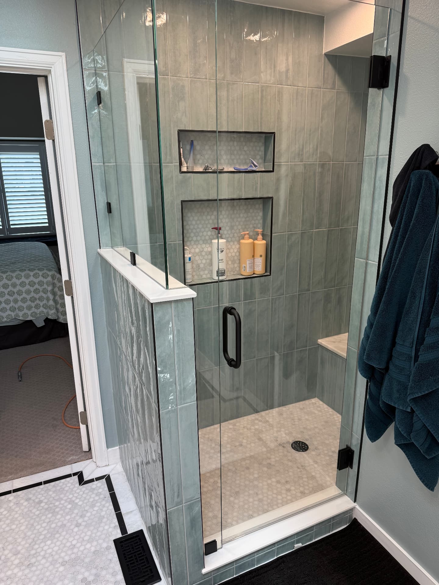 Finished walk-in shower with sea-green vertical tile, niches, and frameless glass door