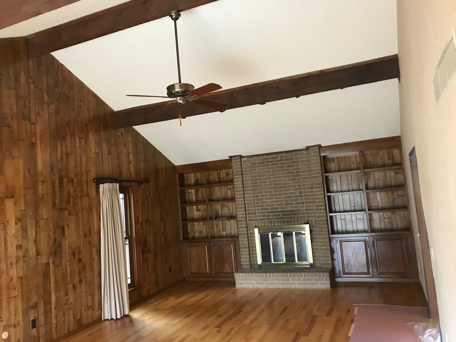 Den with dark wood paneling, brick fireplace, and oak built-ins before remodel