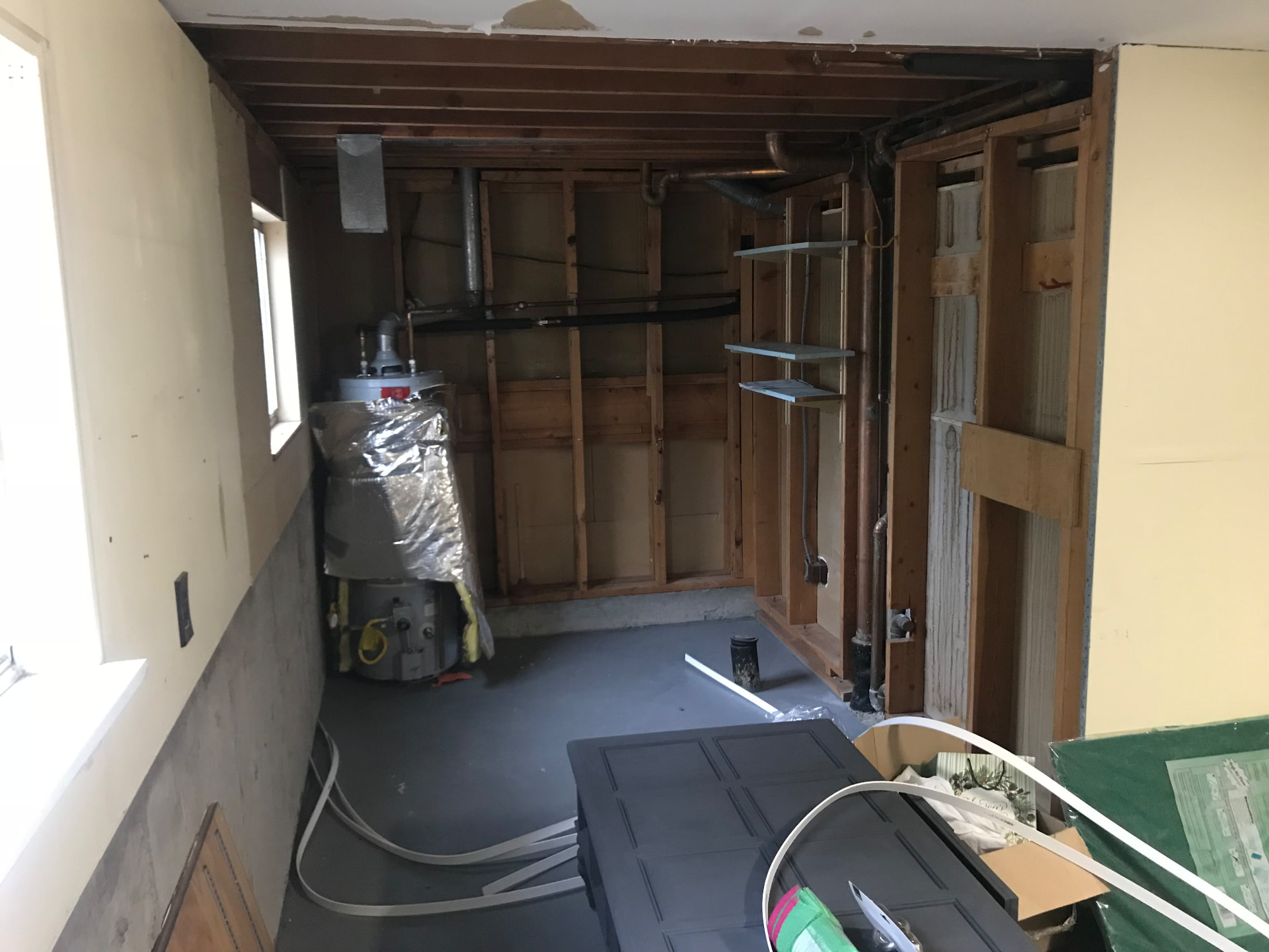 Gutted utility room with exposed framing and water heater before remodel
