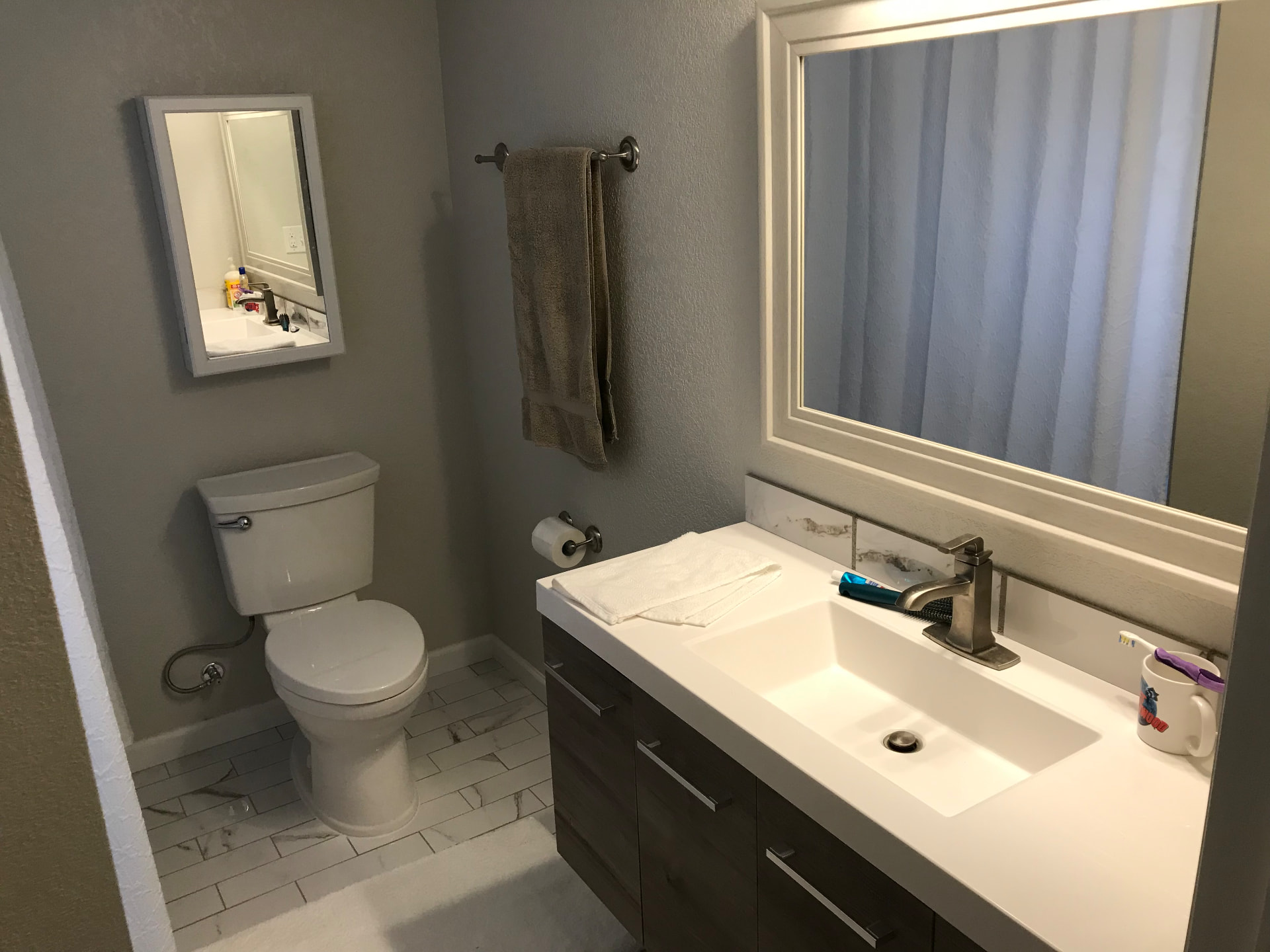 Finished bathroom with dark floating vanity, white counter, and marble-look tile floor