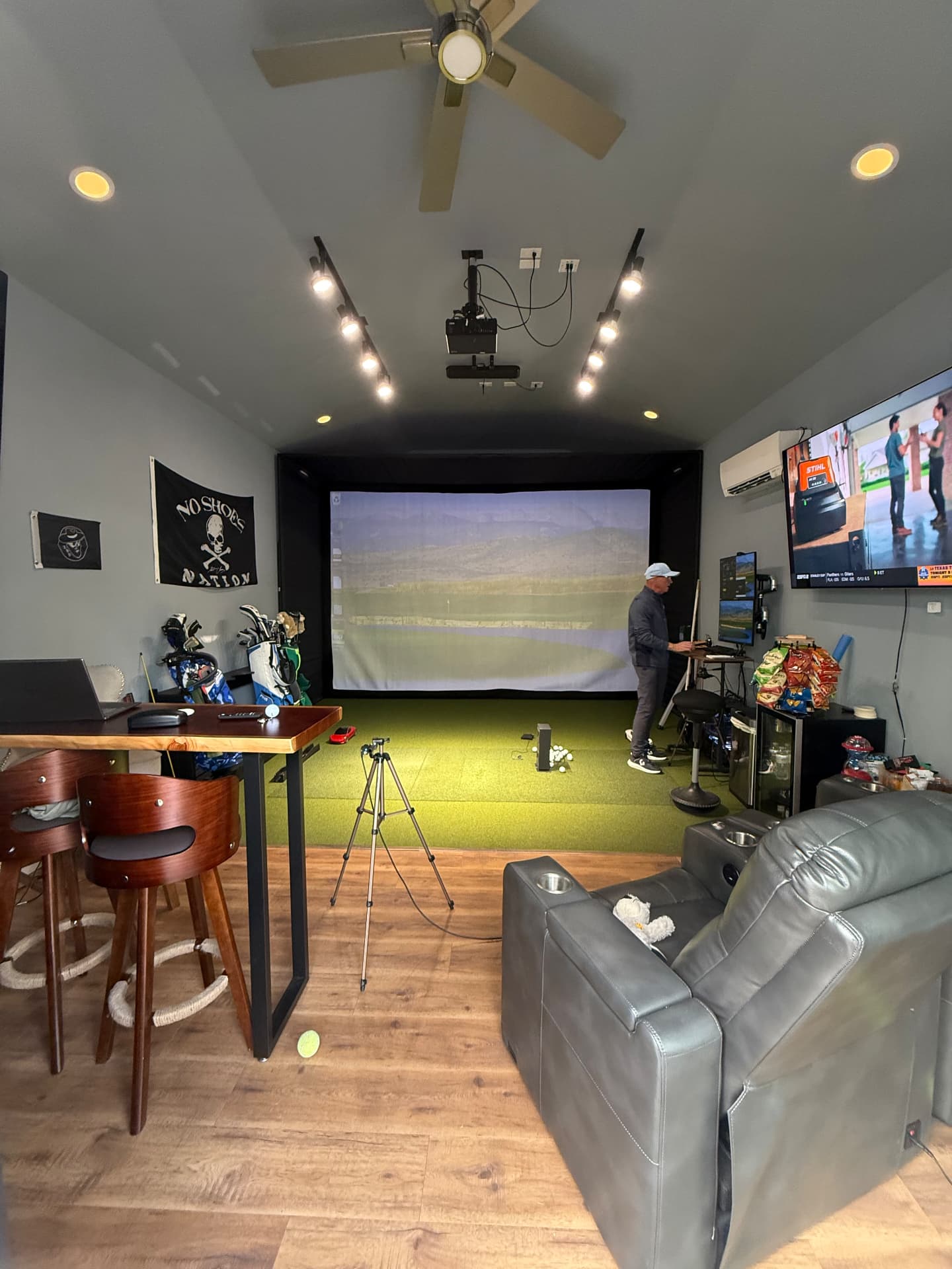 Finished golf simulator studio with screen, bar seating, and recliners