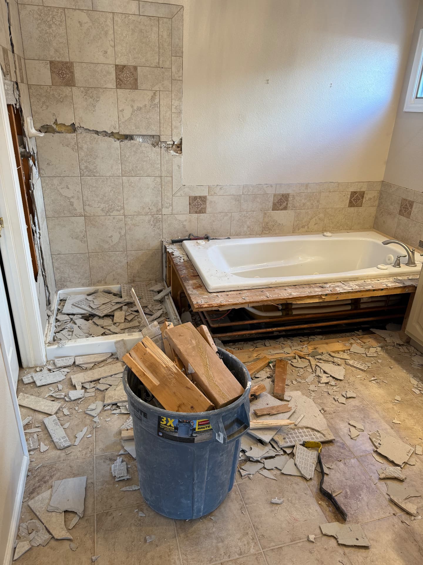 Master bathroom mid-demolition with tile removed around the old tub