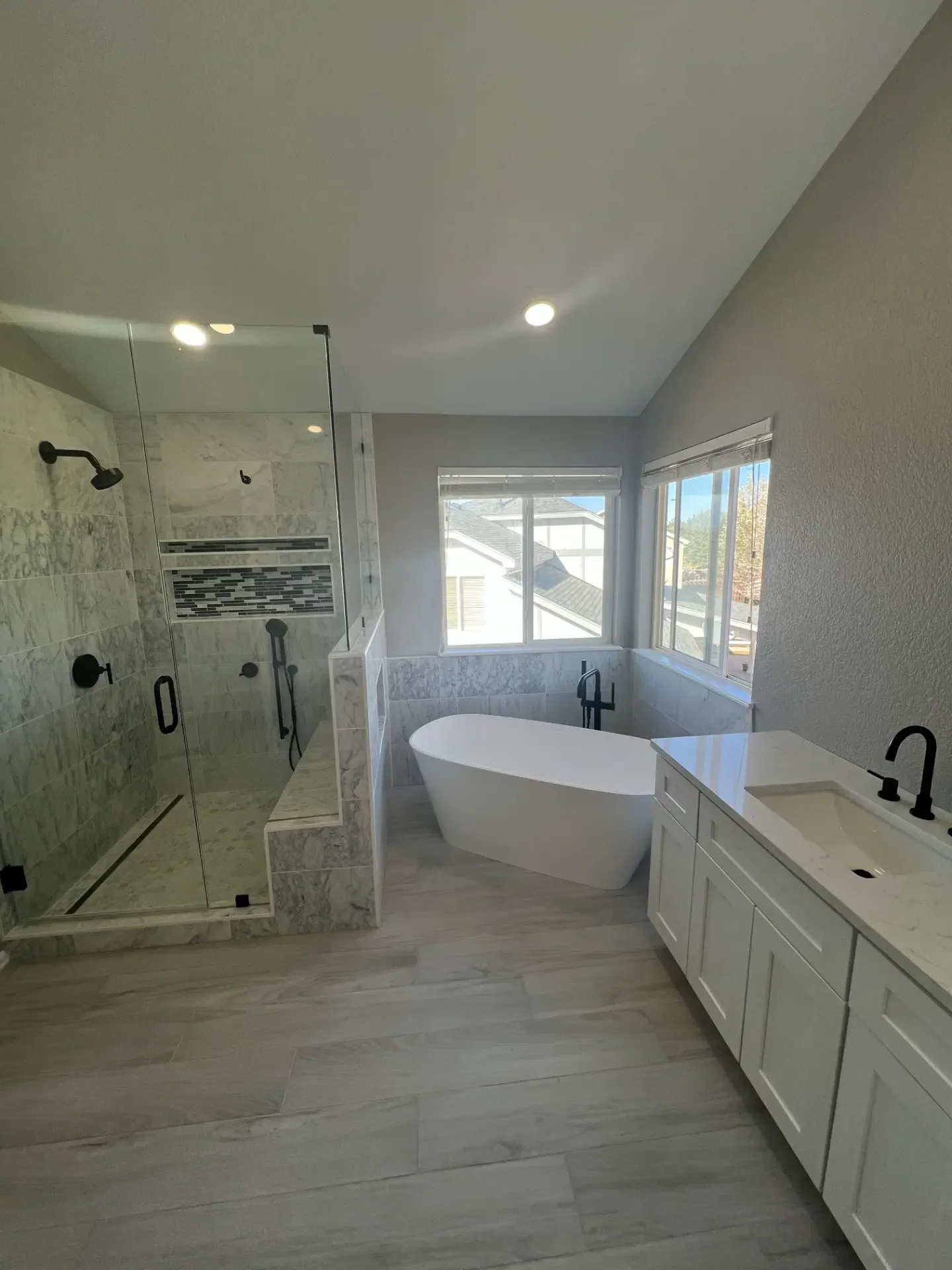 Renovated bathroom with freestanding tub, walk-in shower, and white vanity by JR Burcham