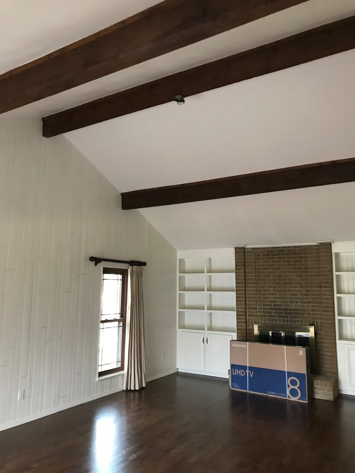 Den with white painted paneling and built-ins, dark stained floors, and exposed beams