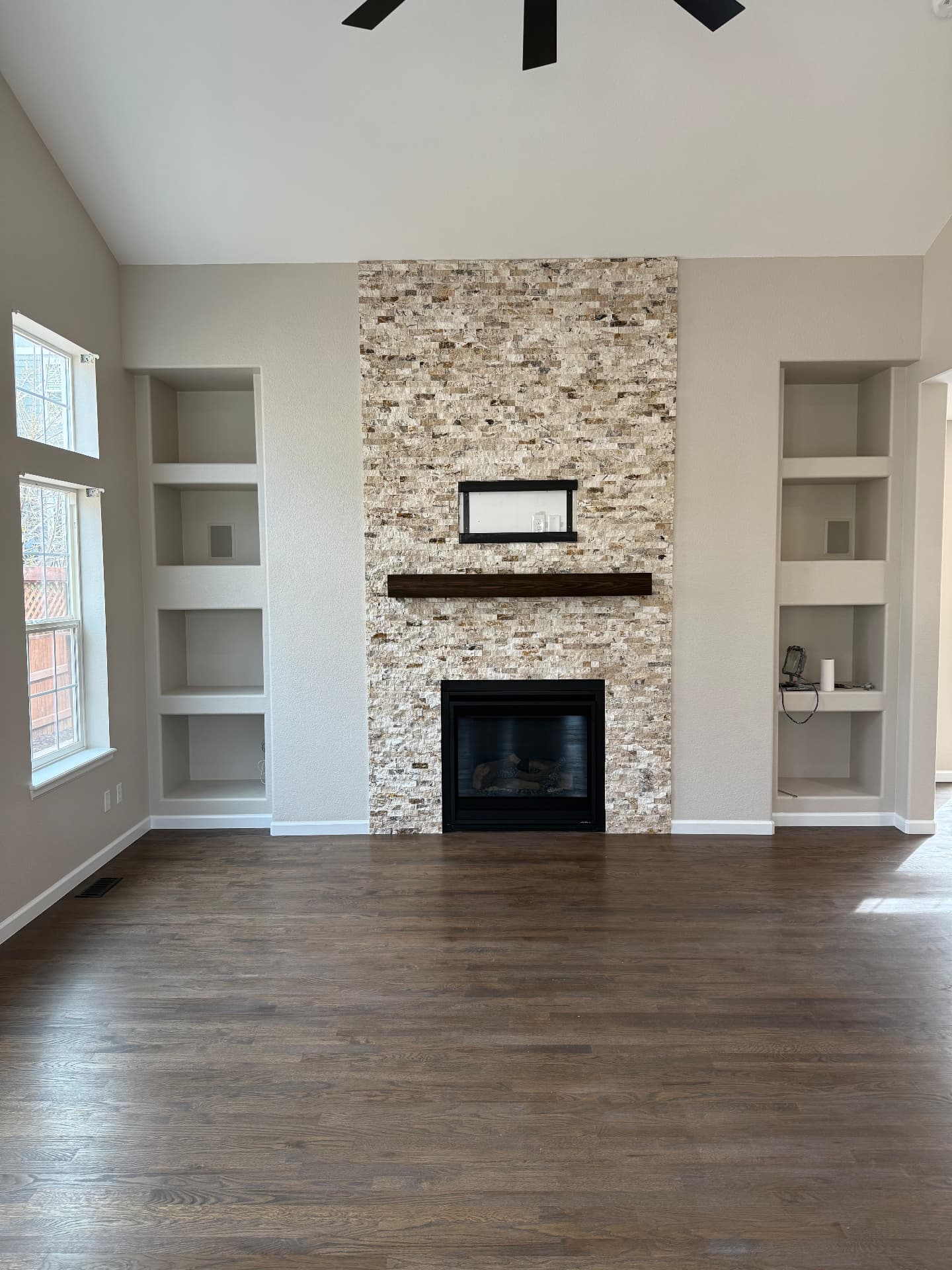 Finished living room with stacked stone fireplace, built-in shelves, and hardwood floors